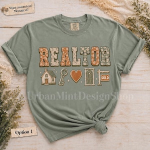 May include: A sage green short-sleeve t-shirt featuring the word REALTOR in large, floral-patterned block letters. Below the text are graphic icons of a house, a key, a heart, a door, and a signpost with the word SOLD printed on it.