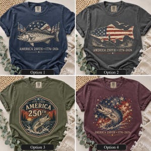 May include: Four short-sleeve t-shirts in navy, charcoal, olive, and maroon. Each features a graphic print with a fish, American flag elements, and the text AMERICA 250TH 1776-2026. The designs include various patriotic motifs like stars, stripes, and lighthouses.