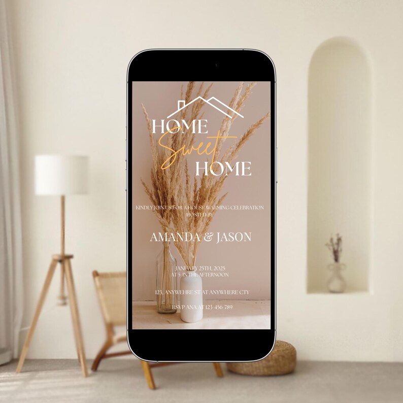 May include: A smartphone displays a housewarming invitation. The design features the text "HOME Sweet HOME" in a script font, with the names "AMANDA & JASON" below. The invitation includes event details and is set against a neutral background with dried floral arrangements.