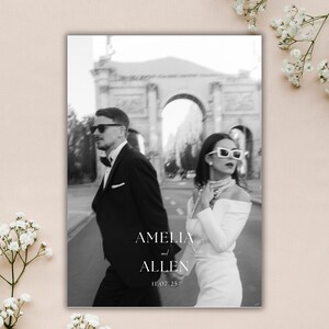 May include: Black and white wedding announcement featuring a couple walking in front of an archway. The text "AMELIA and ALLEN 11.07.25" is displayed in a minimalist font. The couple is wearing sunglasses and formal attire.