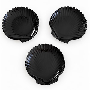 May include: Three glossy black dishes shaped like scallop shells. Each dish features a distinct ribbed texture radiating from the base to the scalloped edge, creating a uniform appearance across all three pieces in this set of decorative tableware.