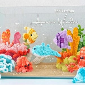 May include: A crocheted aquarium scene with colorful fish, coral, and other sea creatures. The scene includes a yellow and orange fish, a purple fish, a blue dolphin, and various coral formations. The text "Aquarium Wonders" is visible.