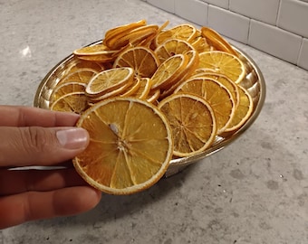May include: A gold-coloured bowl overflowing with dried orange slices. One slice is held up, displaying its texture and colour variations. The oranges are a mix of light and dark orange hues, indicating they are naturally dried.