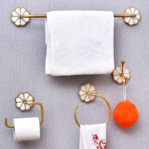 May include: A gold-finished bathroom set including a towel rail, toilet roll holder, towel ring, and hook. Each item has a flower-shaped design with white and gold details. A white towel hangs on the rail, and an orange sponge hangs from the hook.