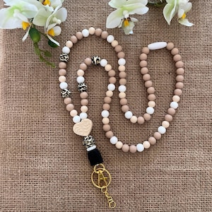 May include: A beaded lanyard in shades of beige, white, and black. The lanyard features a heart-shaped charm and leopard print accents. A gold-coloured clasp and key ring are attached to the bottom. The lanyard is approximately 76 cm long.