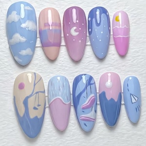 May include: A collection of ten almond-shaped false nails. Each nail features a unique design, including clouds, rainbows, moons, and abstract art in pastel shades of blue, pink, and purple.