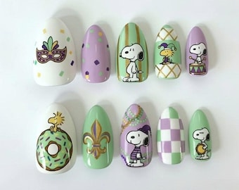 Può includere: Un set di dieci unghie finte ovali con vari disegni. I disegni includono una maschera di Mardi Gras, Snoopy, un giglio e motivi a scacchiera. I colori sono bianco, viola, verde e oro.