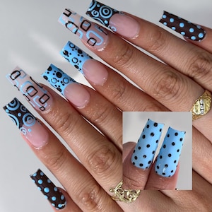 May include: Long, square-shaped acrylic nails with various designs. Some nails feature a light blue base with black polka dots, while others have a nude base with brown and light blue geometric patterns. A small inset shows a close-up of the polka dot design.