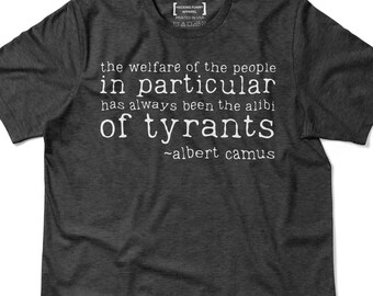May include: Dark gray t-shirt with white text. The text reads "the welfare of the people in particular has always been the alibi of tyrants ~albert camus." The shirt has a crew neck and short sleeves.