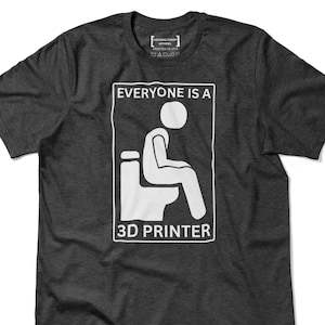 May include: Dark gray t-shirt with a white graphic of a person sitting on a toilet, with the text "EVERYONE IS A 3D PRINTER". The shirt also has the text "HECKING FUNNY APPAREL" and "PRINTED IN USA".