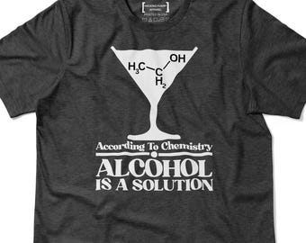 Op de afbeelding: Donkergrijs t-shirt met een witte afbeelding van een martiniglas met een chemische structuur. Daaronder staat de tekst "According To Chemistry ALCOHOL IS A SOLUTION."