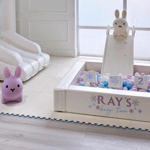 May include: A white inflatable play structure with a slide and ball pit, featuring a bunny theme. The text "RAY'S big TWO" is visible. Includes a purple bunny figure and a white bunny on the slide.