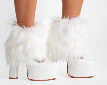 May include: A pair of white platform high-heeled shoes featuring thick block heels and long, shaggy white faux fur cuffs that wrap around the ankles. The shoes have a smooth, solid white finish on the platform soles and the heel structures.