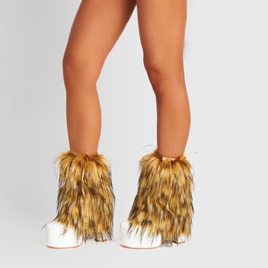 May include: A pair of white platform boots with faux fur trim. The boots have a thick sole and are covered in brown and tan faux fur around the ankles. The boots are designed to be worn on the feet.
