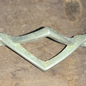 May include: A silver-toned metal drawer pull with a diamond-shaped cutout in the center. The pull has a curved design on each end.