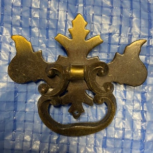 May include: A decorative brass door handle with a floral design. The handle is in the shape of a stylized flower with a ring pull.