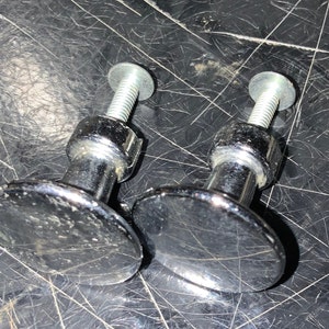 May include: Two chrome cabinet knobs with a round, flat base and a threaded screw. The knobs have a shiny, polished finish.