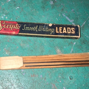 May include: A vintage box of SCRIPTO Smooth Writing LEADS. The box is black with red and white lettering. The leads are in a wooden holder.