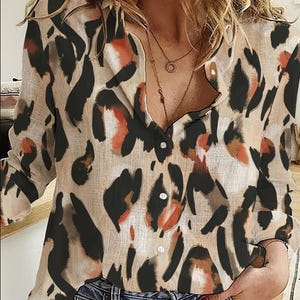 May include: A button-down blouse with a leopard print pattern in shades of beige, black, and orange. The long-sleeved shirt is made of a lightweight material and has a classic collar.