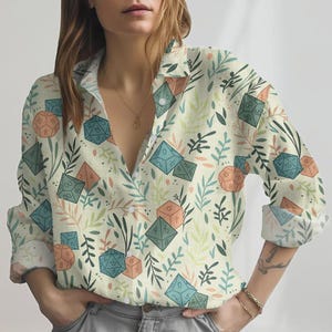 May include: A button-down shirt with a cream background, featuring a pattern of dice and botanical elements in shades of blue, orange, and green. The long-sleeved shirt has rolled-up cuffs.