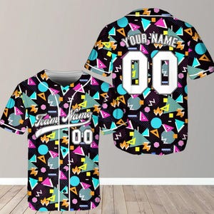 May include: Baseball jersey with a black background and a colourful geometric pattern of triangles, circles, and zigzags. The jersey has the text "Team Name" and the number "00" on the front, and "YOUR NAME" and "00" on the back.