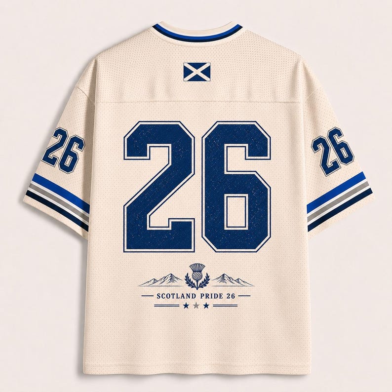 May include: A cream-colored mesh jersey featuring the number 26 in large dark blue font on the back. The design includes a Scottish flag icon, a thistle graphic, and the text SCOTLAND PRIDE 26. The sleeves are accented with blue, grey, and white stripes.