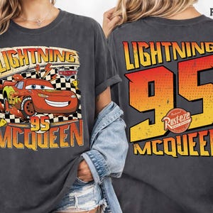 May include: Dark grey t-shirt featuring Lightning McQueen from the Cars film. The front graphic includes McQueen, the number 95, and the text "Lightning" and "McQueen". The back of the shirt displays "Lightning 95 McQueen".