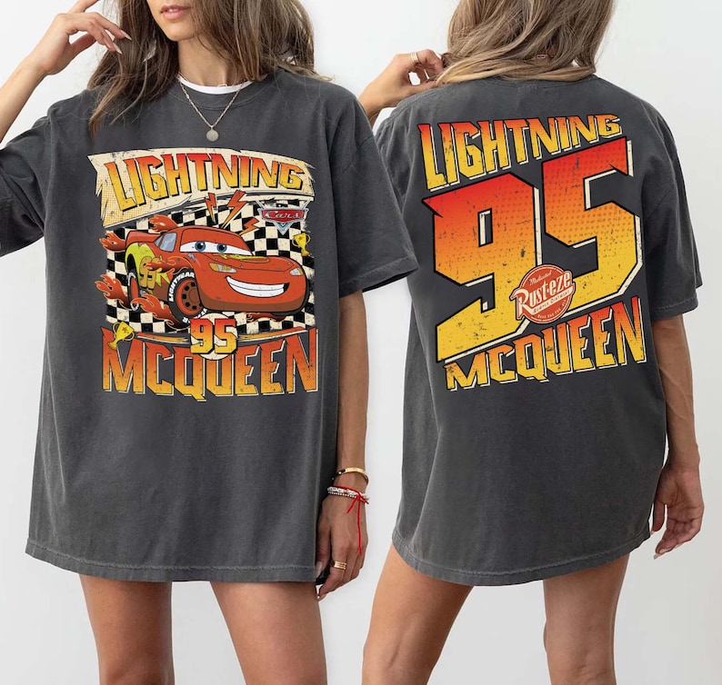 May include: Dark grey Lightning McQueen t-shirt. The front features a graphic of the red race car with the text "Lightning McQueen 95". The back of the shirt displays "Lightning 95 McQueen" in orange and yellow.