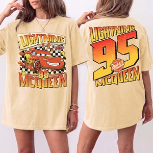 May include: A pale yellow t-shirt with a graphic of Lightning McQueen from the Cars film. The front design includes the text "Lightning 95 McQueen" with a cartoon image of the car. The back of the shirt has a large "95" and "Lightning McQueen" text.