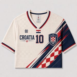 Puede incluir: Una camiseta de cuello en V color crema con el texto CROATIA y el n&uacute;mero 10 en azul marino. La prenda presenta un patr&oacute;n de cuadros rojos y blancos, una peque&ntilde;a bandera croata y un escudo con el texto CROATIA. Rayas azul marino y rojas acent&uacute;an las mangas.