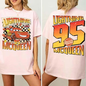 May include: Pale pink t-shirt with a Lightning McQueen design. The front displays McQueen racing with "Lightning 95 McQueen". The back features a large "95" and "Lightning McQueen" text in a retro style.