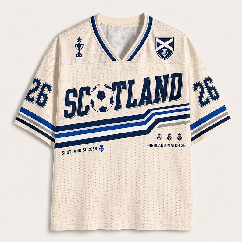 May include: A cream-colored V-neck jersey with blue accents. The front features the text SCOTLAND with a soccer ball as the letter O, the number 26 on both sleeves, a trophy icon, a Scottish flag emblem, and the text SCOTLAND SOCCER HIGHLAND MATCH 26.