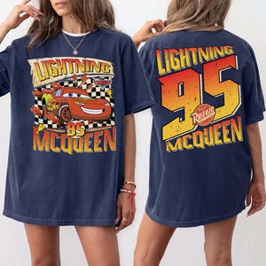May include: Navy blue t-shirt with a Lightning McQueen graphic from the Cars film. The front displays "Lightning 95 McQueen" with a cartoon car. The back features a large "95" and "Lightning McQueen" text in orange and yellow.