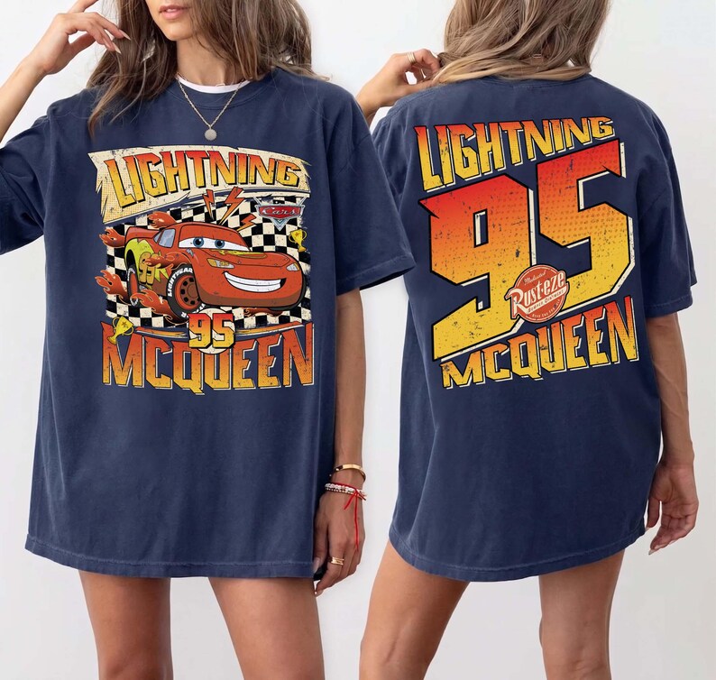 May include: Navy blue t-shirt with a Lightning McQueen graphic from the Cars film. The front displays "Lightning 95 McQueen" with a cartoon car. The back features a large "95" and "Lightning McQueen" text in orange and yellow.