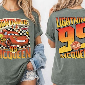 May include: Moss green t-shirt featuring Lightning McQueen from the Cars movie. The front graphic shows McQueen with the text "LIGHTNING 95 MCQUEEN". The back of the shirt displays "LIGHTNING 95 MCQUEEN" in a large, bold design.