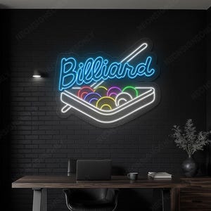 May include: A neon sign reading "Billiard" in a cursive font, with a cue and a rack of billiard balls. The sign is blue and white, mounted on a black brick wall. The room has a desk and a black chair.