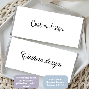 May include: Two rectangular candy bar wrappers with a white background and the black text Custom design printed in a cursive script. The wrappers are displayed on a white tray. The text on the wrappers is clear and legible against the white surface.
