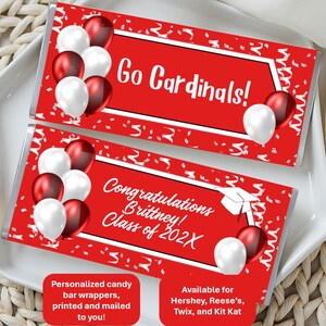May include: Two red candy bar wrappers with white text that reads "Go Cardinals!" and "Congratulations Brittney! Class of 202X." Each wrapper has white and red balloons and confetti. The wrappers are on a white plate.