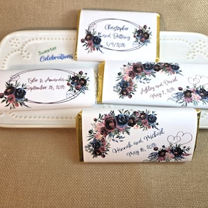 May include: Chocolate bars with floral designs and personalized text for weddings. The bars feature names and dates, with a color palette of burgundy, navy, and pink. They are arranged on a white, decorative tray.