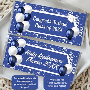 May include: Two candy bar wrappers with blue and white balloon graphics. One wrapper reads "Congrats Joshua! Class of 202X" and the other reads "Holy Redeemer Picnic 20XX". The wrappers are on a white plate.