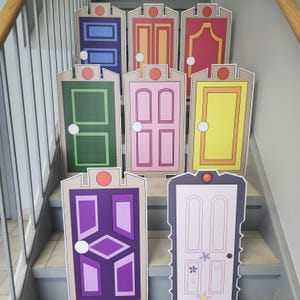 May include: A collection of colorful, cartoon-style door cutouts arranged on a staircase. Each door features a unique design and color scheme, including blue, pink, green, and yellow, with a circular accent at the top. The doors are likely themed for a children's party or event.