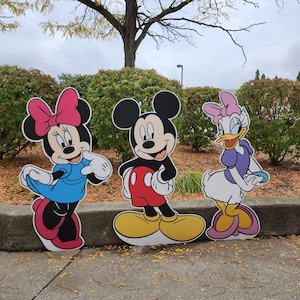 Peut inclure: Découpes en carton de Mickey Mouse, Minnie Mouse et Daisy Duck. Mickey Mouse porte un short rouge et des chaussures jaunes. Minnie Mouse porte une robe bleue et un nœud rose. Daisy Duck porte un haut et un nœud violets.