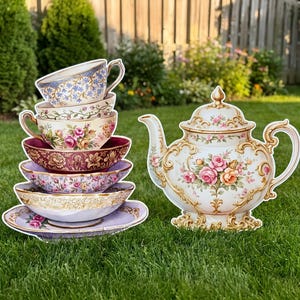May include: A stack of ceramic teacups and saucers featuring various floral patterns in blue, pink, and gold, positioned next to a matching porcelain teapot with a lid, ornate gold trim, and a central bouquet of pink and yellow roses.