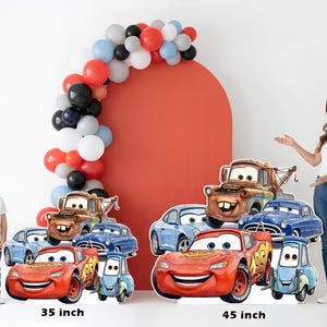 May include: Cardboard cutouts of Cars movie characters, including Lightning McQueen, Mater, and others, in various sizes. A red arch with a balloon garland and two people are also in the image. The larger cutout is 45 inches tall, and the smaller is 35 inches.