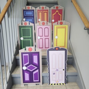 May include: A collection of colorful, cartoon-style door cutouts, each with unique designs and colors, including blue, orange, red, green, pink, and yellow. The doors are arranged on a staircase, suggesting a decorative or themed display.