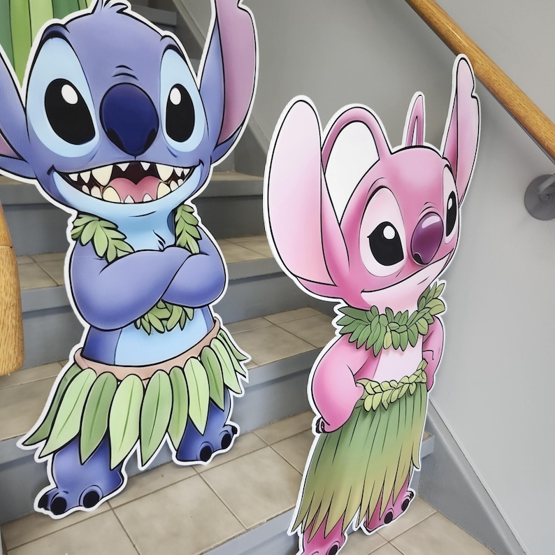 May include: Two cartoon character cutouts, one blue and one pink, stand on a staircase. The blue character has its arms crossed and wears a leaf skirt. The pink character has its arm raised and wears a leaf skirt. Both have large ears.