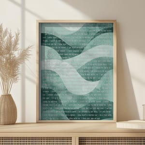 Puede incluir: Una impresión enmarcada con un diseño de olas turquesas y blancas, llena de texto. La obra de arte está en un marco de madera clara y se encuentra sobre una superficie de madera. También se ve un jarrón con plantas secas y una taza.