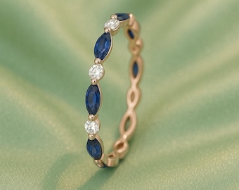 May include: A rose gold ring with a repeating pattern of marquise-cut blue sapphires and round white diamonds. The ring is set against a soft green background, creating a contrast that highlights the gemstones.