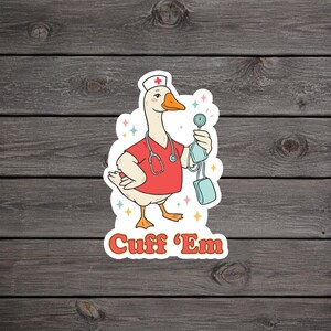 May include: A sticker featuring a cartoon goose dressed as a nurse, wearing a red uniform and a white hat with a red cross. The goose is holding a blood pressure cuff and stethoscope. The text "Cuff 'Em" is written in orange letters.