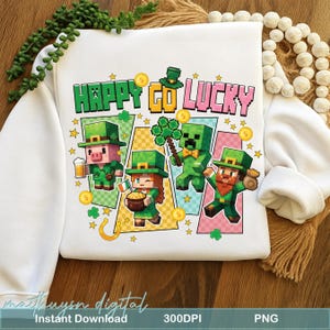 Pode incluir: Camisola branca com um gráfico colorido com personagens pixelizados vestidos para o Dia de São Patrício. O design inclui o texto "HAPPY GO LUCKY", moedas de ouro, estrelas e uma ferradura. Os personagens incluem um porco, uma menina, um creeper e um duende.